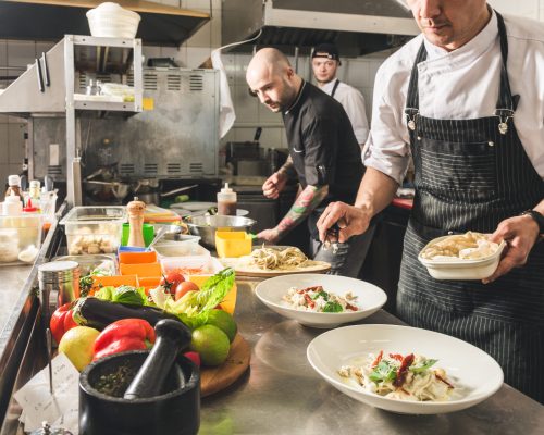 Professional chef cooking in the kitchen restaurant at the hotel, preparing dinner. A cook in an apron makes a salad of vegetables and pizza